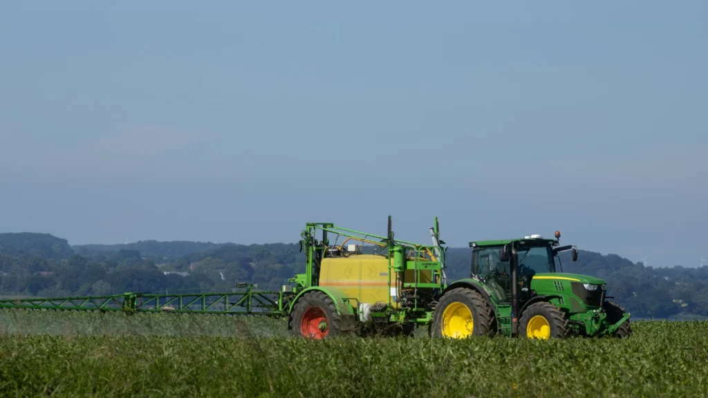 A tractor dispersing microbial fertilizer across a vast farm field.